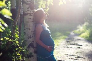 Woman pregnant and leaning against tree