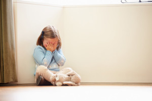 Unhappy Child Sitting On Floor In Corner At Home