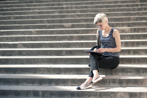 Young blonde woman using tablet while sitting on steps of Trocad