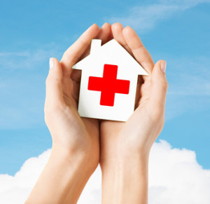 hands holding paper house with red cross