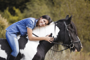 attractive brunette female rider embracing her horse and smiling