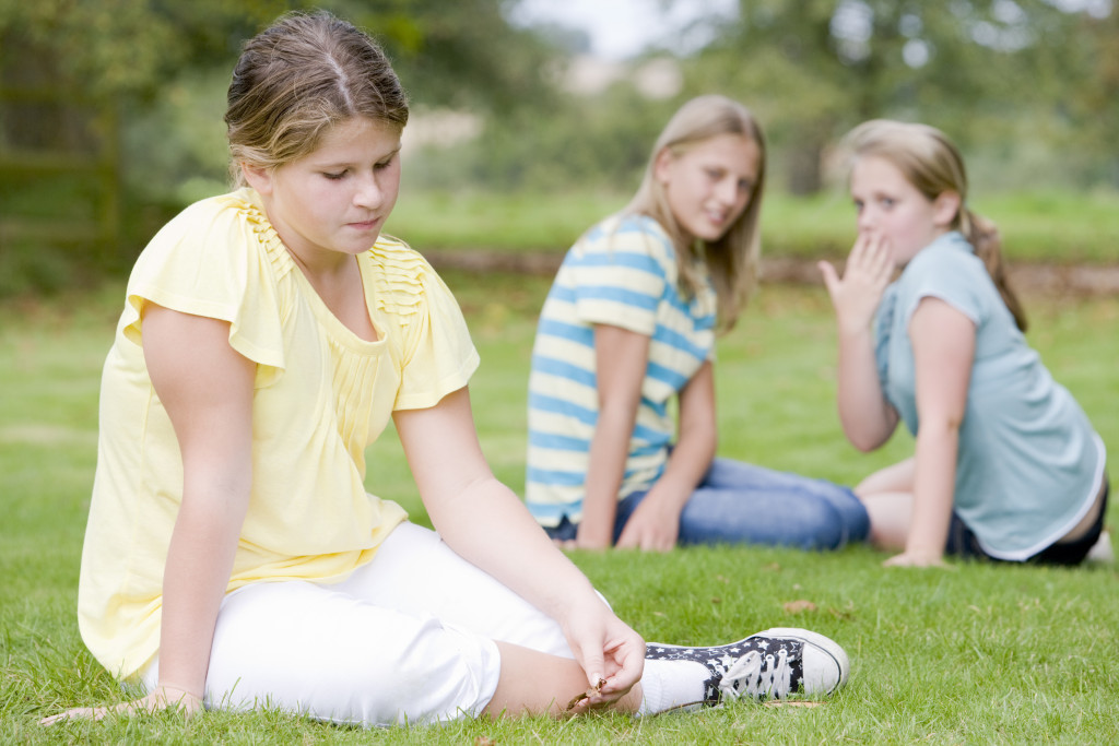 Two young girls bullying other young girl outdoors