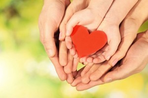 Red heart in family hands on bright background