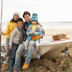 Family Group Sitting On Boat With Fishing Rod On Winter Beach