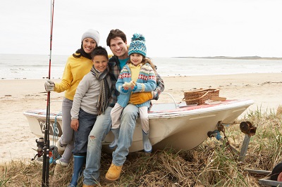 Family Group Sitting On Boat With Fishing Rod On Winter Beach