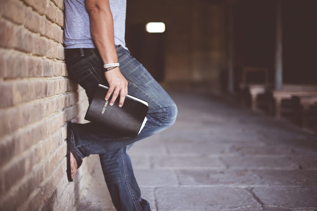 Man leaning against a wall holding a book on Prevalence & Features of Eating Disorders in Males