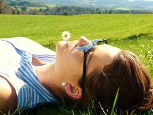 Lady laying in field with a daisy in her mouth